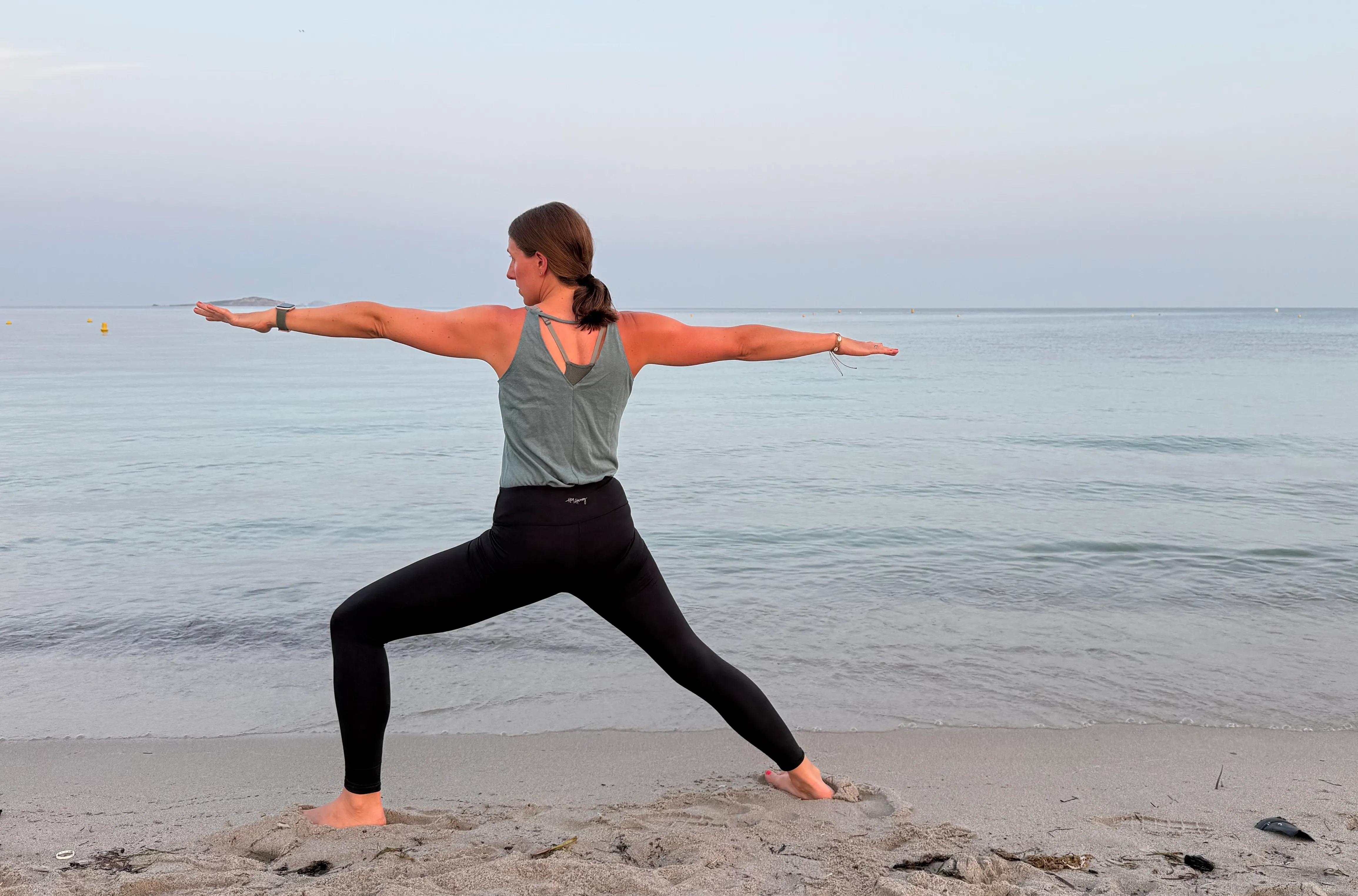 Yogalehrerin im Krieger II am Meer, Blick zur Weite